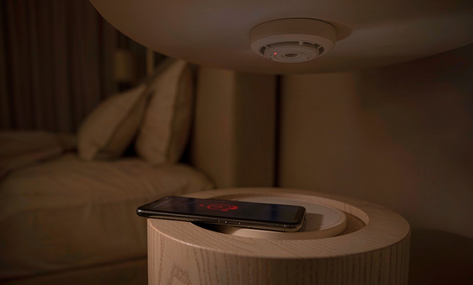 Smartphone showing a smoke alarm push notification with a connected alarm in the background
